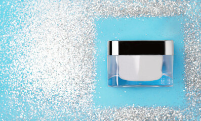 Beauty face cream container on a festive bluebackdrop with shimmering silver glitter. For holiday skincare campaigns, luxury beauty product advertising, and Christmas-themed promotions.