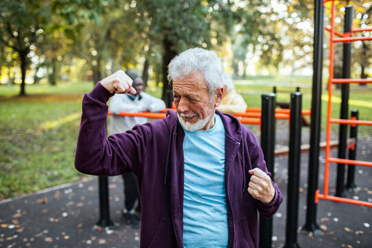 Senior man flexing muscles at outdoor gym in sunny park