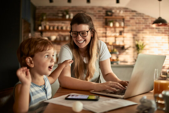 Mom working on laptop while spending time with toddler at breakfast table
