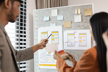 A man and a woman are looking at a table with a lot of cards and a laptop. The cards are about UX...