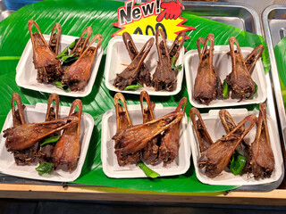 Deep fried duck mouth tongues with sesame on plastic plates at vendor's stall at street market in Thailand. A popular treat among tourists. Top view