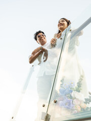 Joyful Asian bride and groom share a romantic moment outdoors, basking in the sunlight sky with scenic view. Their love and happiness radiate, beautiful wedding day and celebration of romance.
