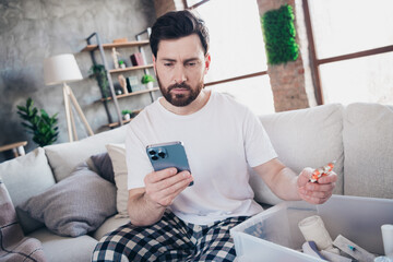 Photo of nice young man hold device pills wear pajama wake up enjoy modern cozy interior flat...
