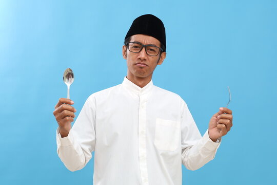 Sad confused asian muslim man holding spoon and frok with unhappy face expression