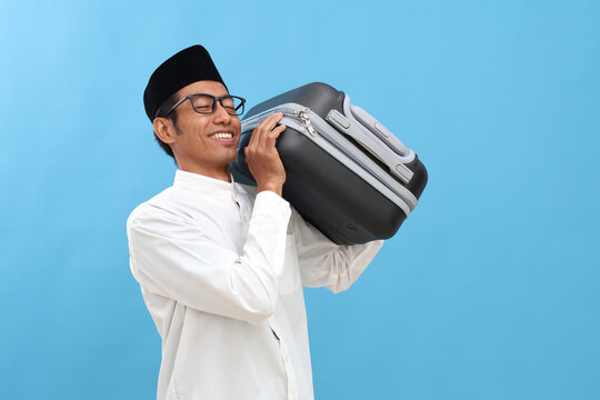 Excited asian muslim man standing while carrying travel suitcase. Going mudik or travel to hometown for Ramadan eid mubarak celebration