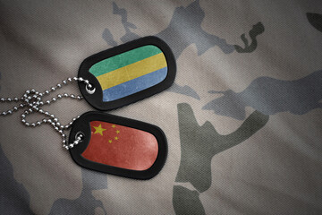 vintage army blank, dog tag with flag of gabon and china on the khaki texture background. military...