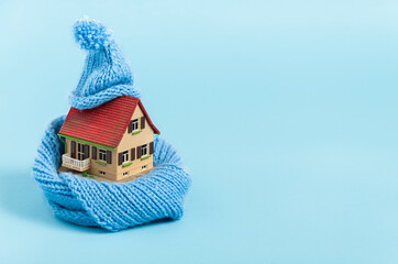 thermal insulation of buildings: old miniature model house with blue scarf and bobble hat, blue background