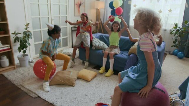 Birthday boy and his girl friend jumping on hopper balls while celebrating with company of gen alpha children in living room