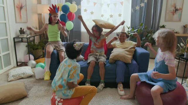 Zoom out view of two gen alpha kids bouncing on hopper balls competing with each other, three friends raising hands while cheering for them at birthday party
