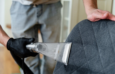 A person wearing gloves is using a vacuum attachment to clean the upholstery of a chair. The bright...