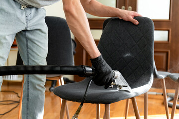 A person wearing gloves is using a vacuum attachment to clean the upholstery of a chair. The bright...