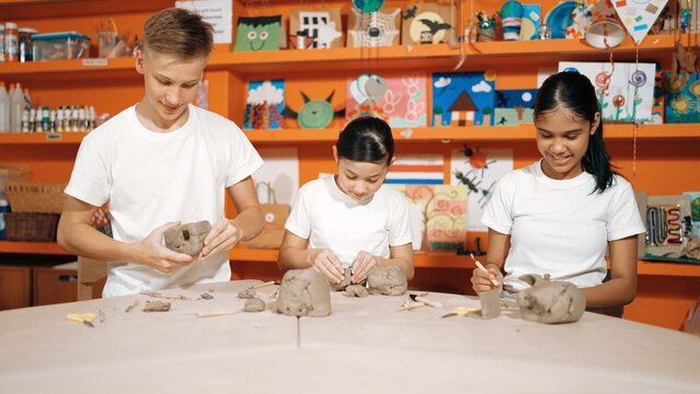 Smart boy modeling cup of clay with happy friend at pottery workshop. Skilled diverse highschool student working and modeling dough while laugh at happy child at art lesson. Creative art. Edification.