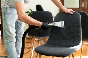 A person wearing gloves is using a vacuum attachment to clean the upholstery of a chair. The bright...