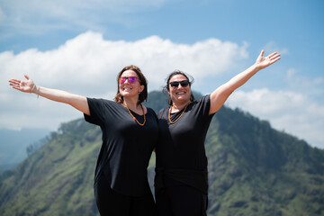 Two smiling women raising arms enjoying sri lanka landscape