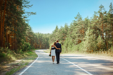 Newlyweds are walking along an asphalt road in a pine forest. The concept of a long happy life for...