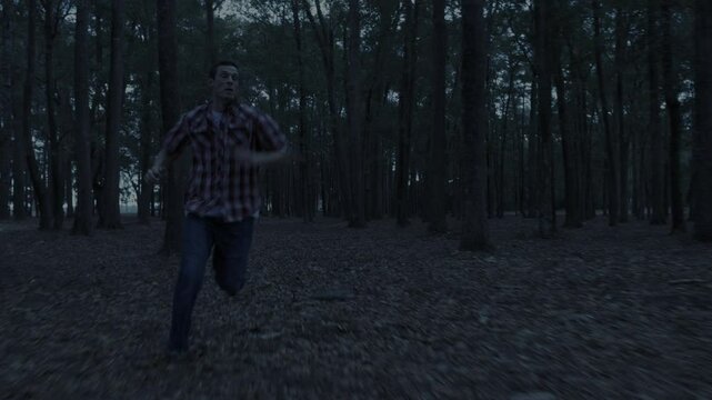 Man running away from unknown threat at night in a dark forest.