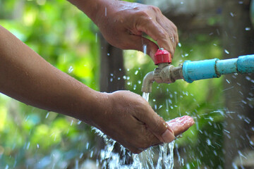 Hands Washing Under Outdoor Faucet with Flowing Water in Natural Green Background
