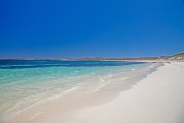 Fototapeta premium Idyllic beach with turquoise waters and rocky shoreline on Rottnest Island under a bright blue sky