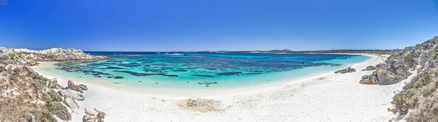 Obraz premium Idyllic beach with turquoise waters and rocky shoreline on Rottnest Island under a bright blue sky