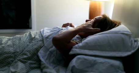 Older woman in bed at night yawning, tired person preparing to sleep