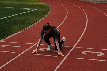 Determined female athlete in starting position on running track, ready for a race.  Focus on ambition and achievement. High-quality image perfect for sports, fitness, and motivation themes.
