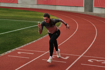 Fototapeta premium Female athlete in starting position on running track. Ready to sprint. Dynamic action shot showcasing determination and speed. Perfect for sports, fitness, and healthy lifestyle themes.