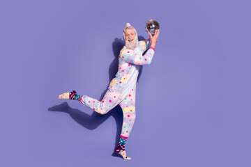 Happy man in colorful unicorn pajama poses with disco ball on purple background