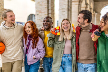 Fototapeta premium Happy multiracial group of friends walking hug on city street - Cheerful young people hanging outside together after college - Friendship concept with guys and girls having fun outdoors weekend