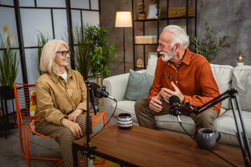 senior man host and woman guest sit on sofa and record a podcast