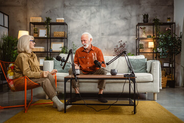 senior man host and woman guest sit on sofa and record a podcast
