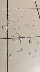 Broken kitchen glassware on a tiled floor. Sharp shards scattered in all directions. Top view