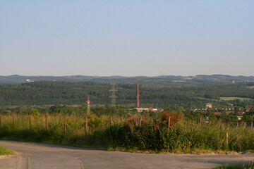 Small forest covered hill view with industrial features like electricity lines and tall chimney, ...