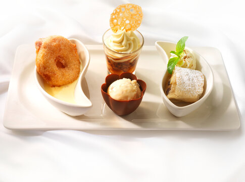 Dessert Men&uuml;, Dessert Telller mit Apfelstudel Vanilleeis im Schokoladen Becher gebackenem Ananasring und Eiskaffee mit Vanille Sahne Tupfer.
