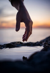 beautiful female hand touches the surface of the water with her fingers in the beautiful sunset...