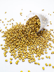 Gold color masterbatch granules spilled from the cup and isolated on white background,color pigment carrier polymer in plastic industry.Perfect for plastic company catalog design.