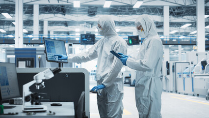 Two Scientists in Sterile Suits Walking In Electronics Factory Research Center. Technician With...