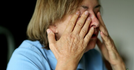 Fototapeta premium Tired person rubbing face with hands. Older lady rubs eyes
