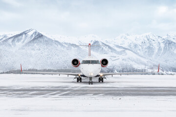 Naklejka premium Front view of a passenger regional jet taxiing at winter airport on the background of high scenic mountains