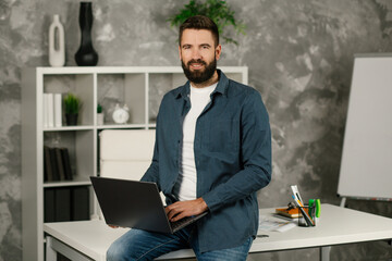 Portrait of a handsome smiling businessman holding laptop at coworking office. Successful worker, career advance.