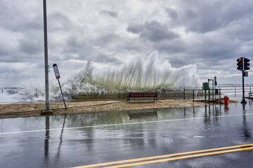 Large waves crashing into the streets and flooding it.