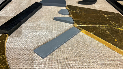 Modern abstract art close-up with textured gold, black, and gray elements on a beige burlap fabric...