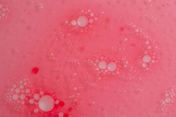 White and red oil drops in water as a background. Pink solution and background. Little drops group around bigger ones, creating a floral pattern.