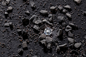 Ein einzelner brillant geschliffener Diamant, verborgen unter dunklen Kieseln und Sediment,...