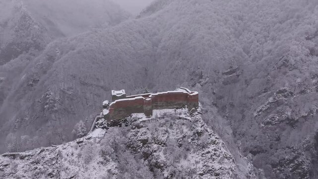 Poenari fortress in Romania during winter snowfall. Aerial 4K video with this important historical landmark for Dracula castle in the mountains. Poenari Castle on top of Fagaras Mountains.