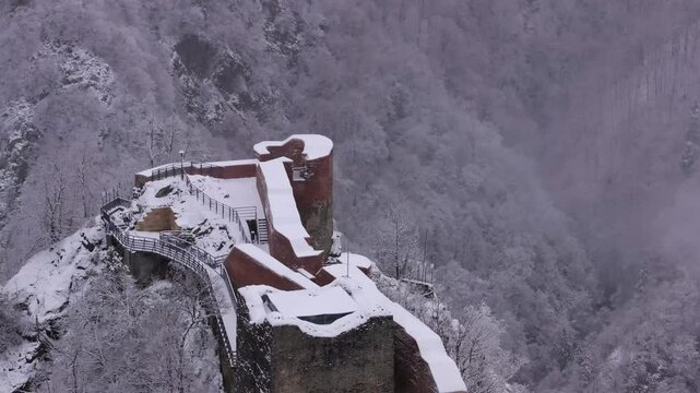 Poenari fortress in Romania during winter snowfall. Aerial 4K video with this important historical landmark for Dracula castle in the mountains. Poenari Castle on top of Fagaras Mountains.