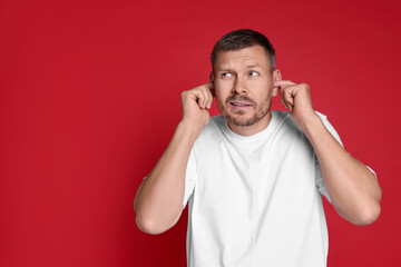 Man covering his ears with fingers on red background, space for text