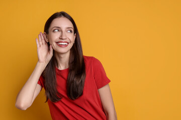 Woman showing hand to ear gesture on orange background, space for text