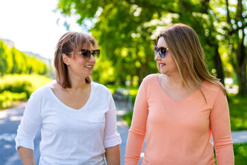 Portrait of two mature beautiful women walking and talking in city park on spring day