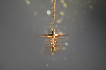 Hypnosis session. Golden pendulum swinging on grey background, motion blur effect. Magic lights