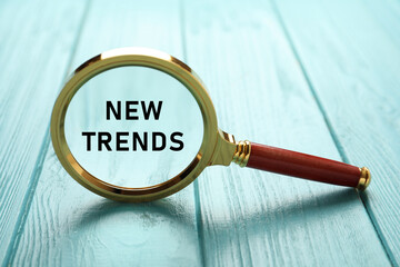 Words New Trends in magnifying glass on turquoise wooden table, closeup. Concept of searching for...